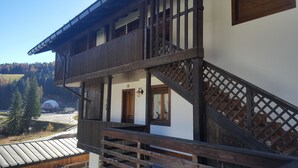 En traditionel bjælkehytte med en træbalkon, en dør og et vindue med gardiner.