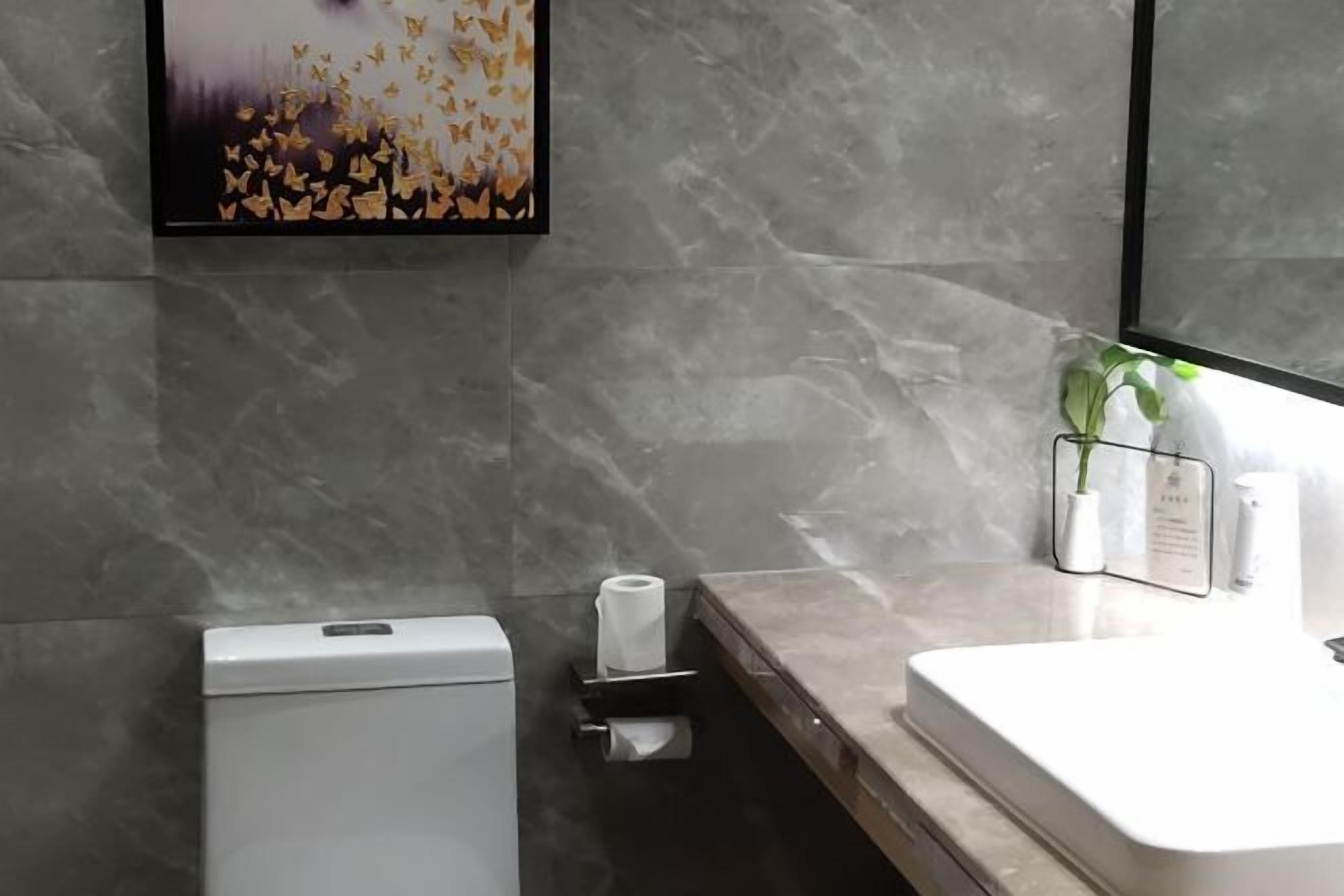 A modern bathroom with a marble wall, a toilet, a sink, and a framed artwork above the toilet.