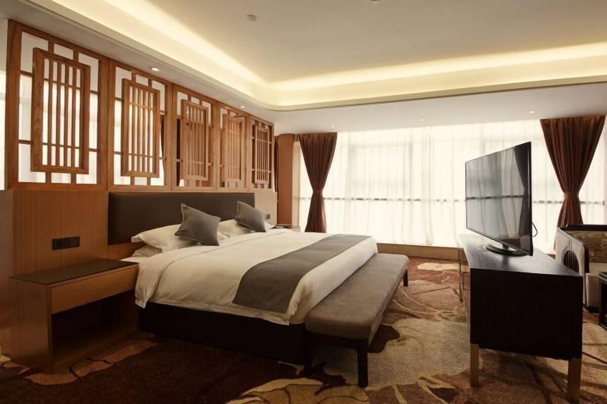 A modern hotel room with a large bed, a desk with a flat-screen TV, and a decorative wooden panel wall.