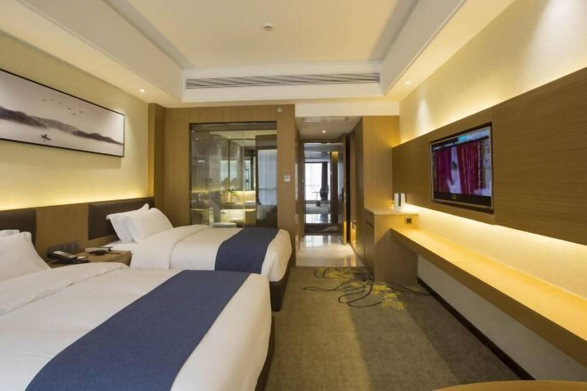 Une chambre d’hôtel avec deux lits, un bureau, une télévision et une vue sur le couloir.