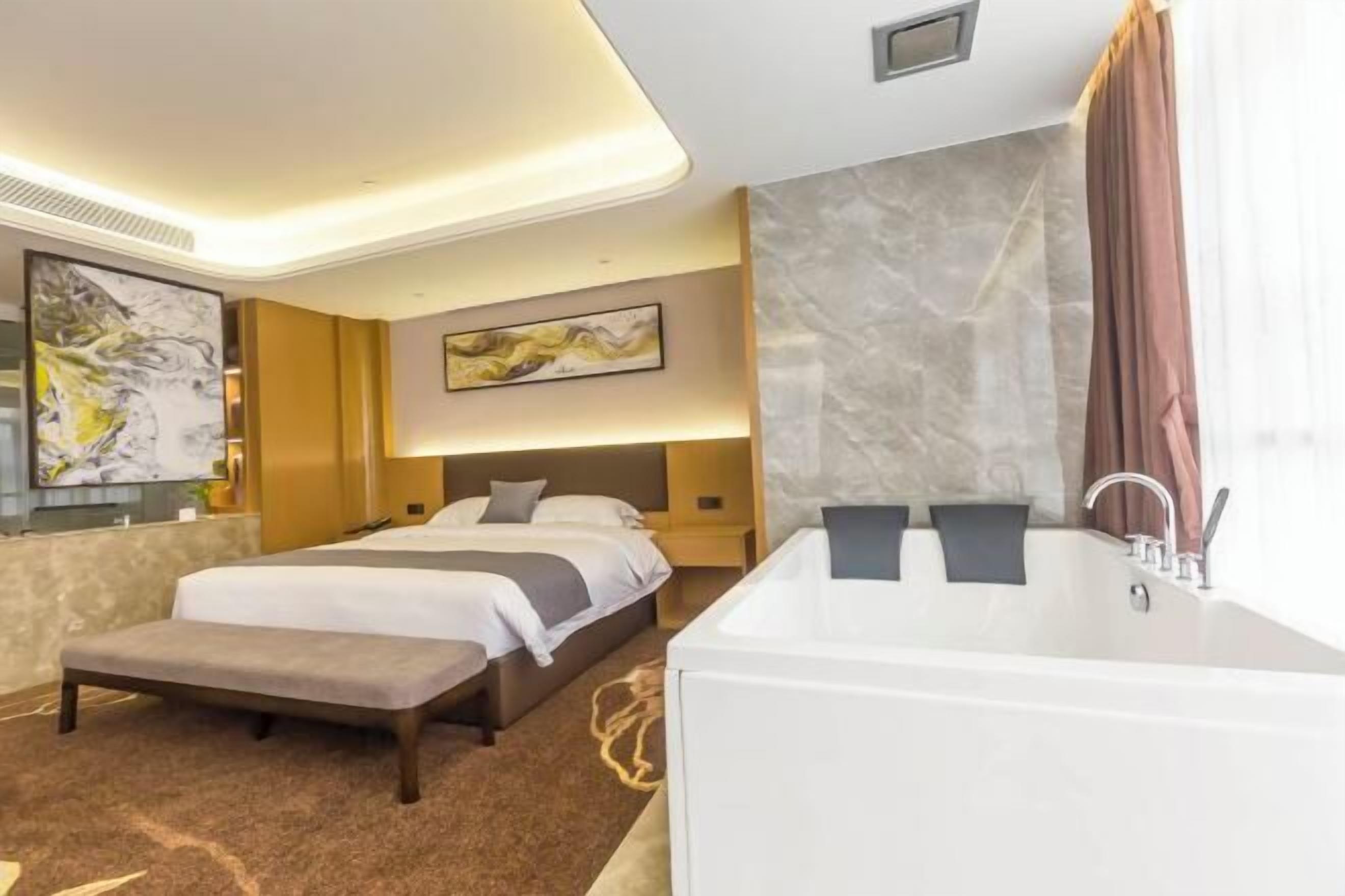 A modern hotel room with a large bed, a separate seating area, a bathtub, and a marble wall.