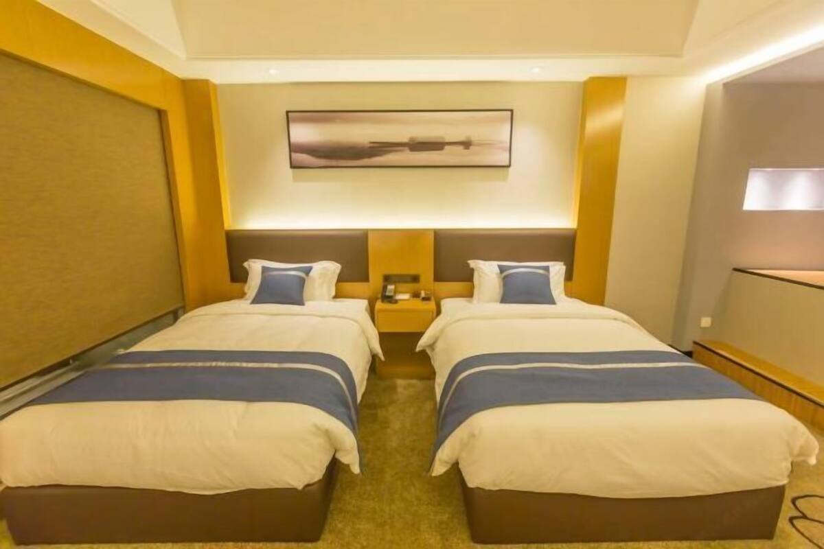 A hotel room with two beds, a large window, and a painting on the wall.