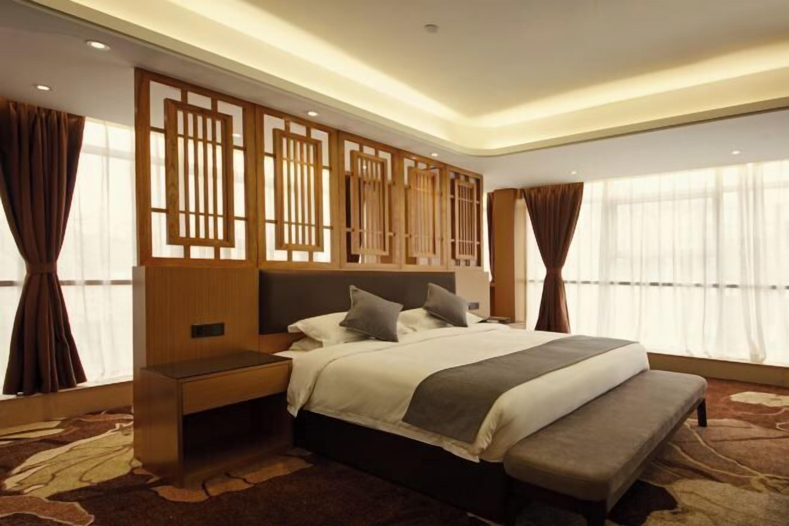 A modern hotel room with a large bed, a wooden headboard, and a bench at the foot of the bed.