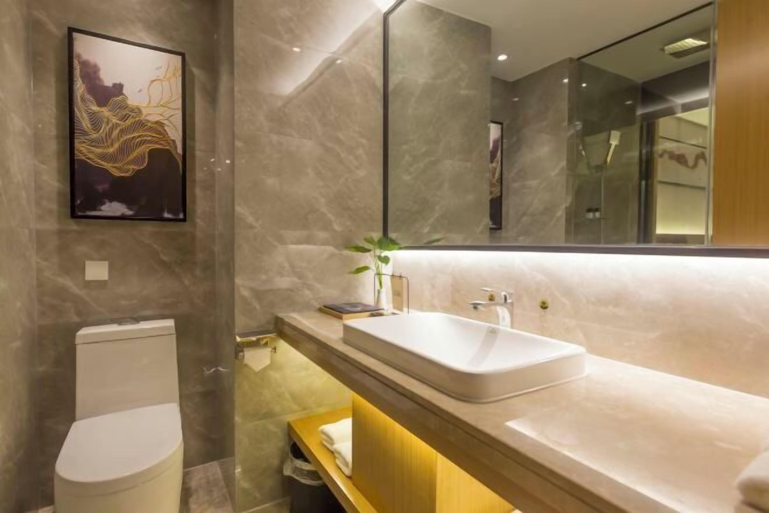 Une salle de bain moderne avec un mur en marbre, des toilettes blanches, un grand miroir et un lavabo avec un meuble-vasque en bois.
