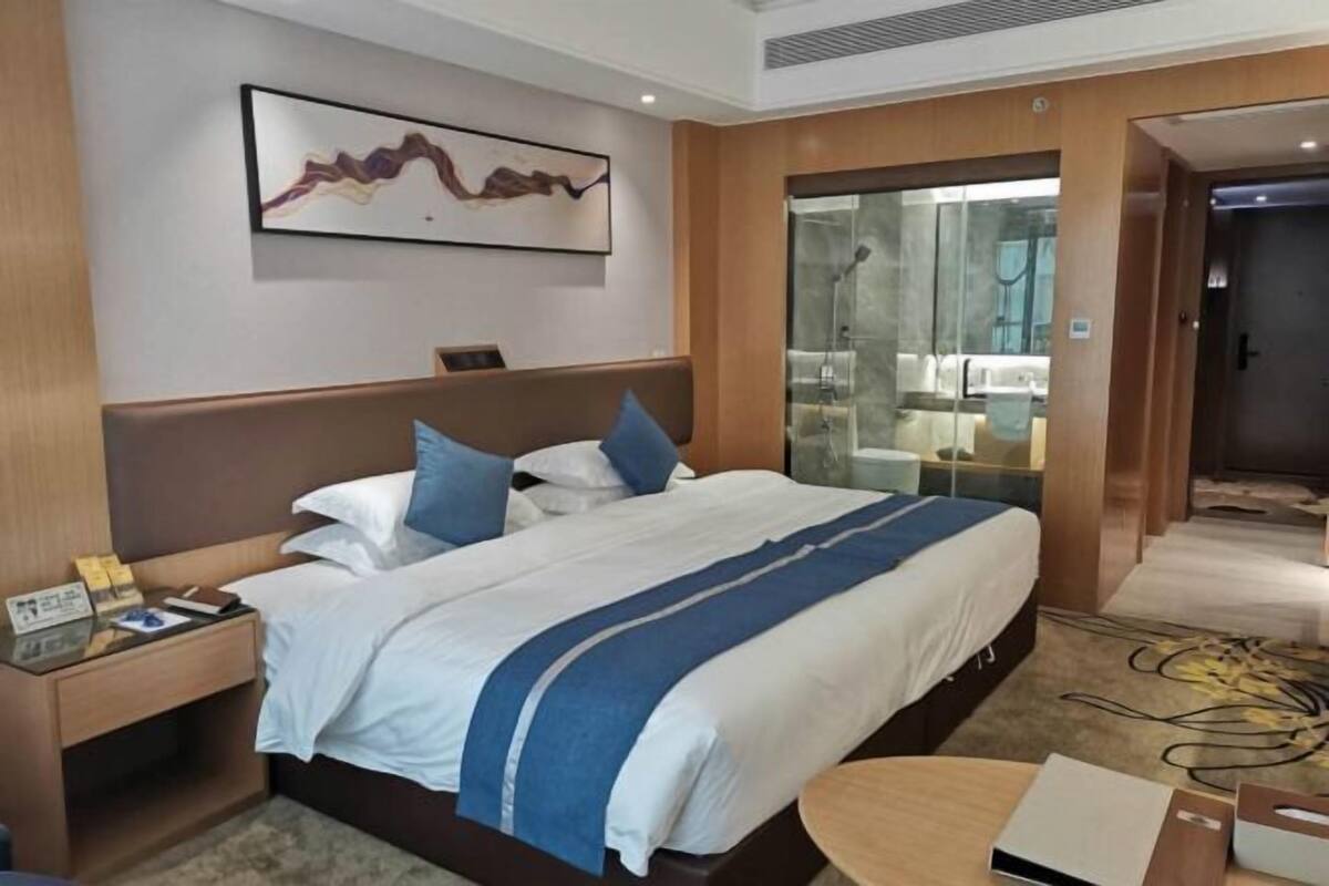 Une chambre d’hôtel avec un grand lit, une table de chevet, un bureau et une cabine de douche en verre.