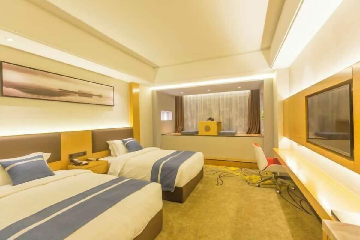 Une chambre d’hôtel avec deux lits, un bureau, une chaise, une télévision et une fenêtre avec des rideaux.