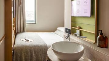 A hotel room with a bed, a large mirror, a sink, and a window.