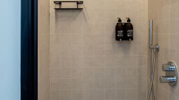 A shower with a handheld showerhead, a handheld shower attachment, and two bottles of shampoo and conditioner on a shelf.