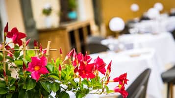 Une salle avec des tables dressées pour le dîner, une plante aux fleurs rouges au premier plan et un arrière-plan flou qui évoque un cadre hôtelier.