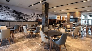 Un restaurante moderno con suelo de mármol, mobiliario contemporáneo y un mural de montañas en la pared.