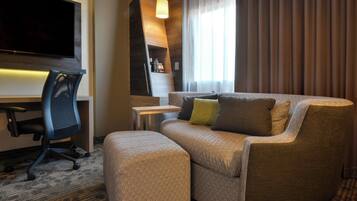 A modern hotel room with a sofa, ottoman, and a desk with a chair.