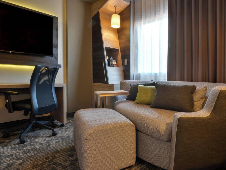 Et moderne hotelværelse med sofa, skammel og skrivebord med stol.