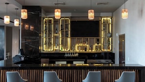 Un área de bar moderna con mostrador negro, respaldo de listones de madera y cuatro taburetes de bar.