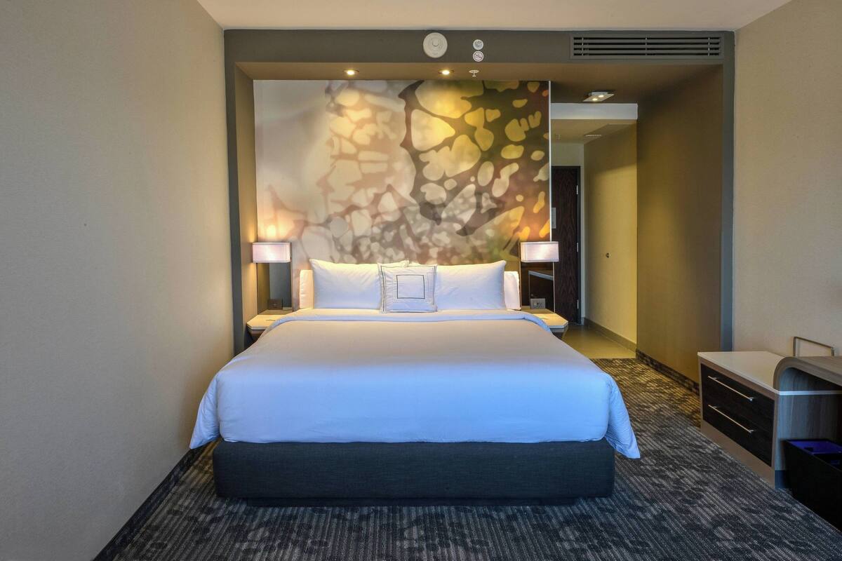 Ein Hotelzimmer mit einem großen Bett, zwei Nachttischlampen, einem Nachttisch und einer Wand mit strukturierter Gestaltung.