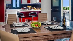 Un espace repas moderne avec une table en bois dressée pour quatre personnes, un saladier rempli de salade et une bouteille de vin posée sur la table.