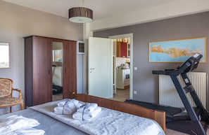 A bedroom with a bed, a treadmill, a wardrobe, a chair, and a map on the wall.