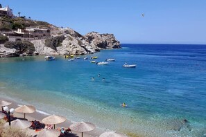 Une plage côtière aux eaux bleues et limpides, avec des bateaux et des parasols.