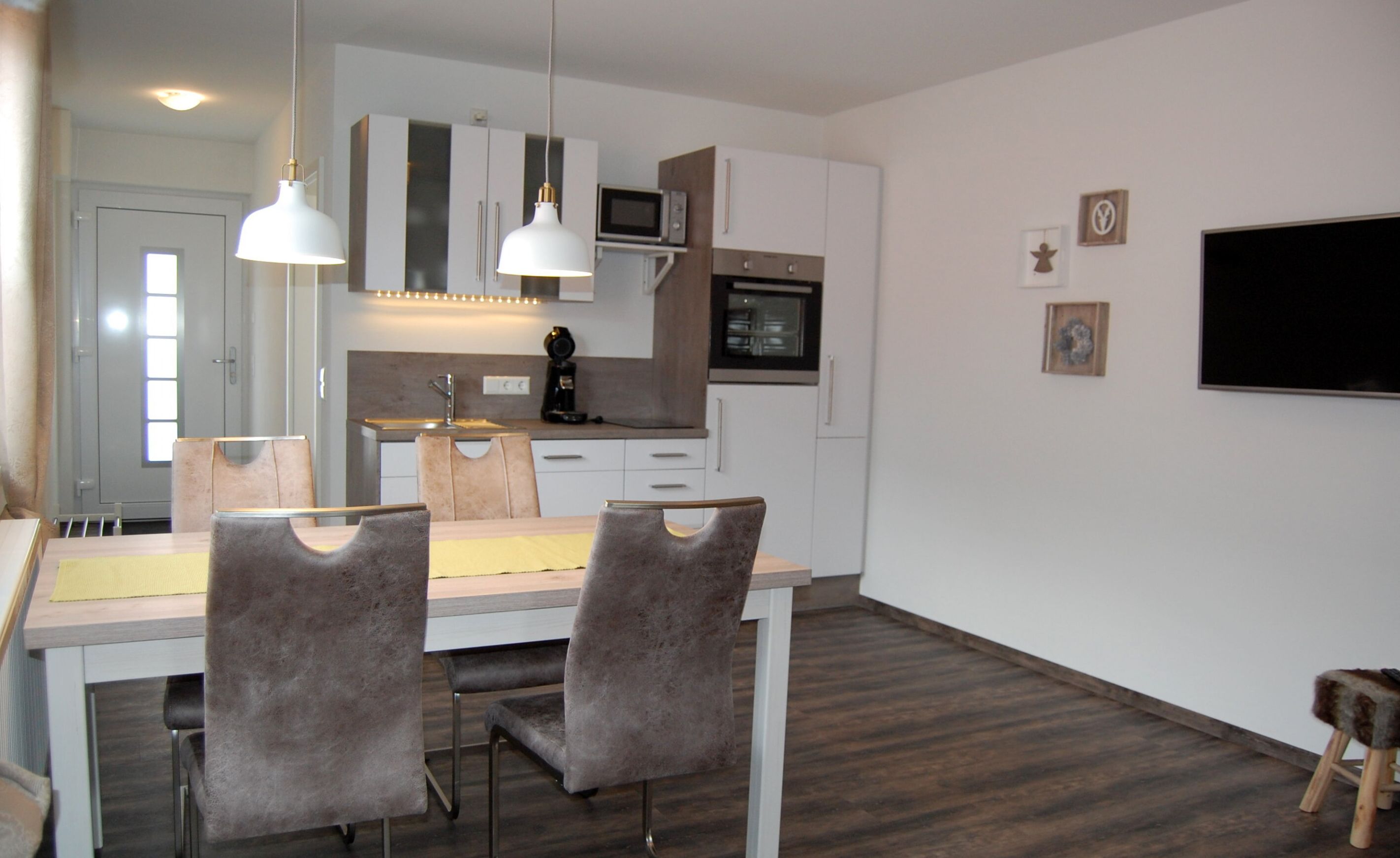 A modern kitchen with white cabinets, a microwave, and a coffee maker. There are two chairs and a table in the dining area.