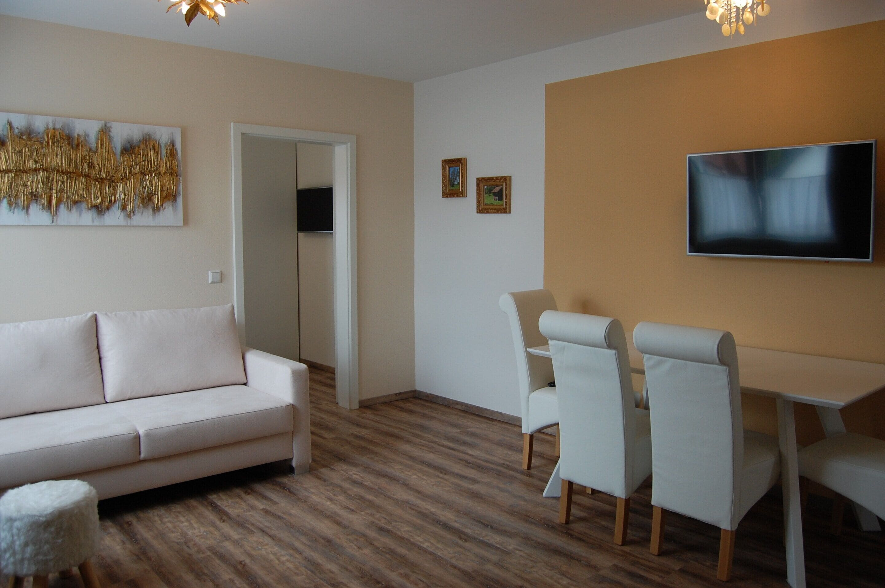 A modern living room with a sofa, chairs, a TV, and artwork on the walls.