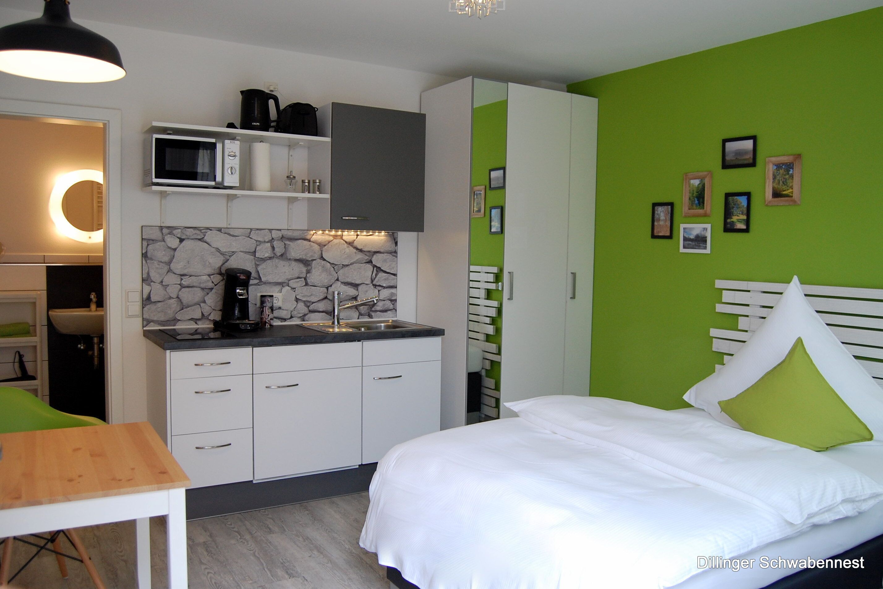 A modern bedroom with a bed, green walls, and a stone backsplash in the kitchenette.