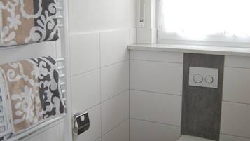 Un bagno piccolo e moderno con il water, un portasciugamani con asciugamani fantasia, un termosifone e una finestra vista esterna.