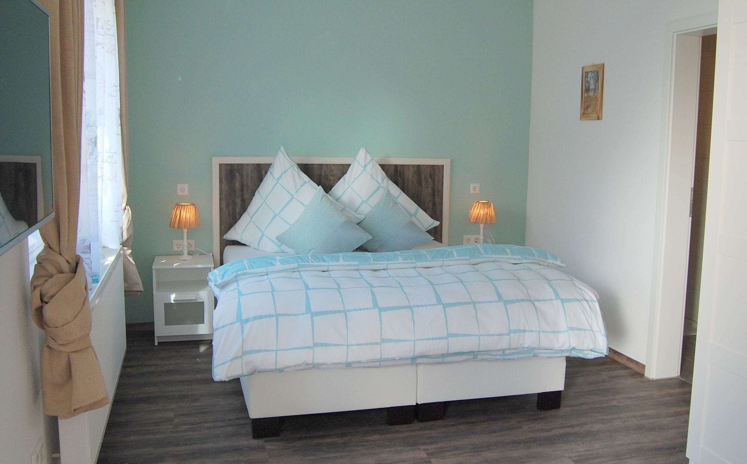 Een slaapkamer met een bed, twee nachtkastjes, een houten hoofdeinde en een aan de muur hangend schilderij.