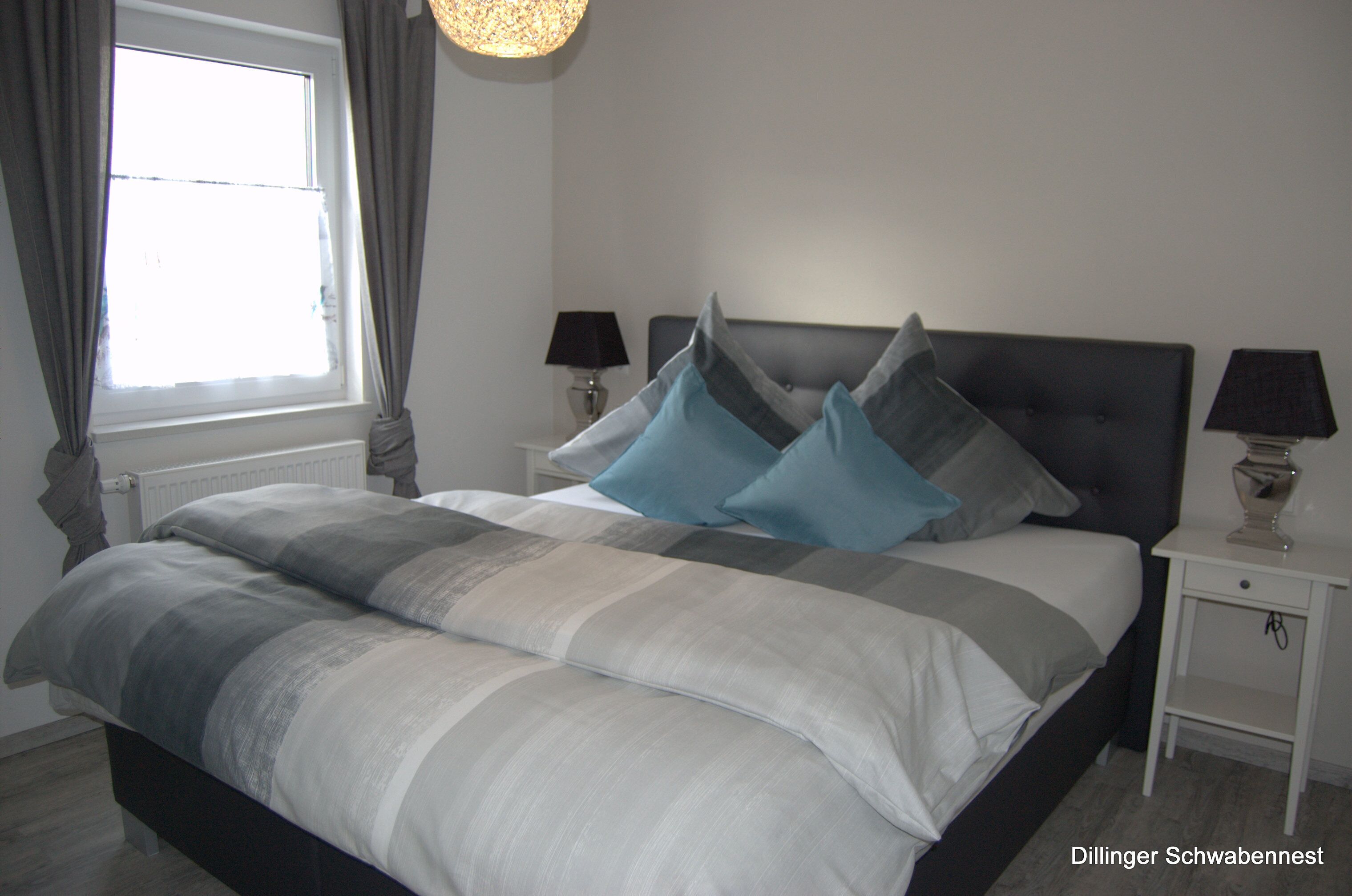 A neatly made bed with grey and white bedding, two bedside tables with lamps, and a window with curtains.
