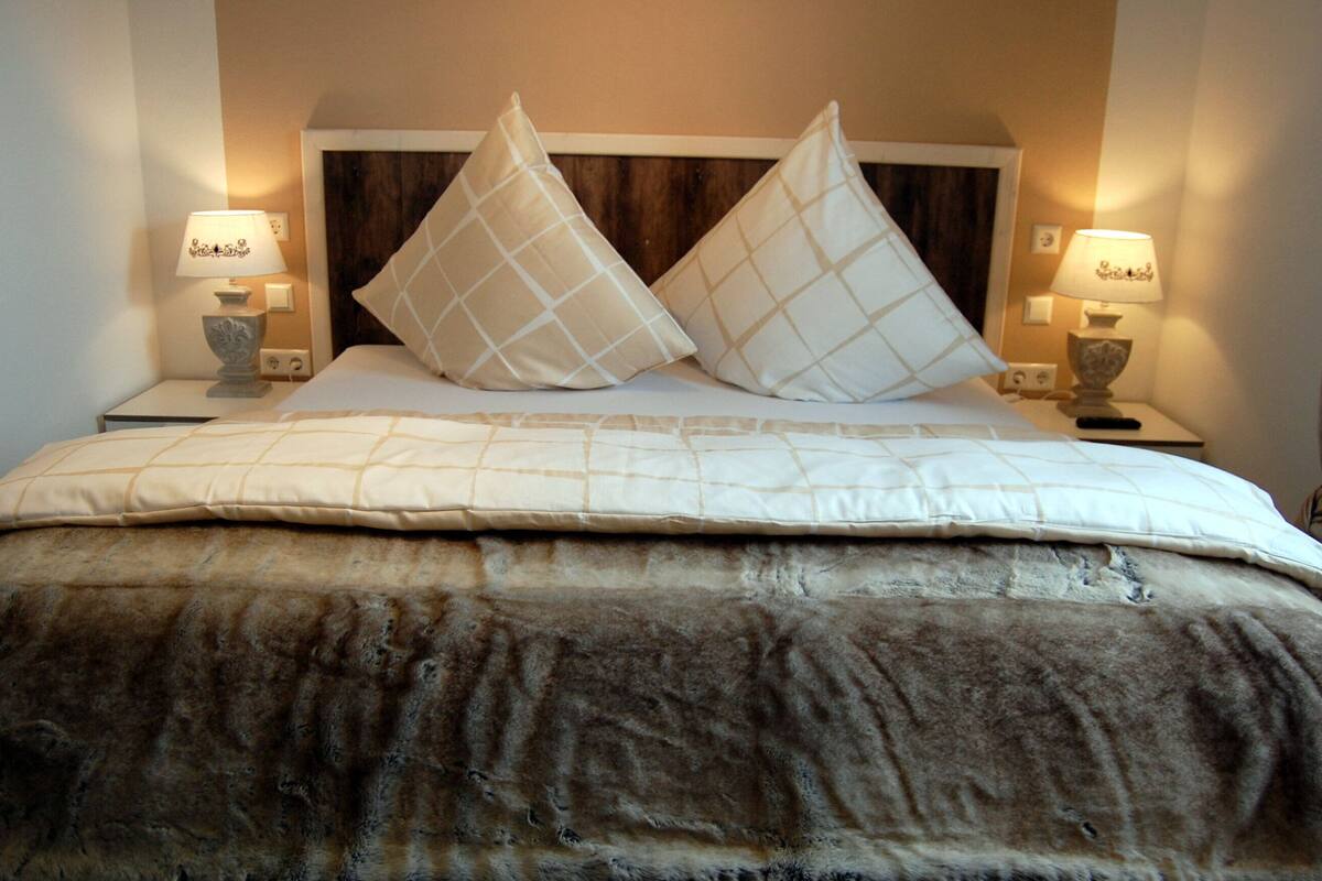 A bed with a headboard, two bedside lamps, and a blanket.