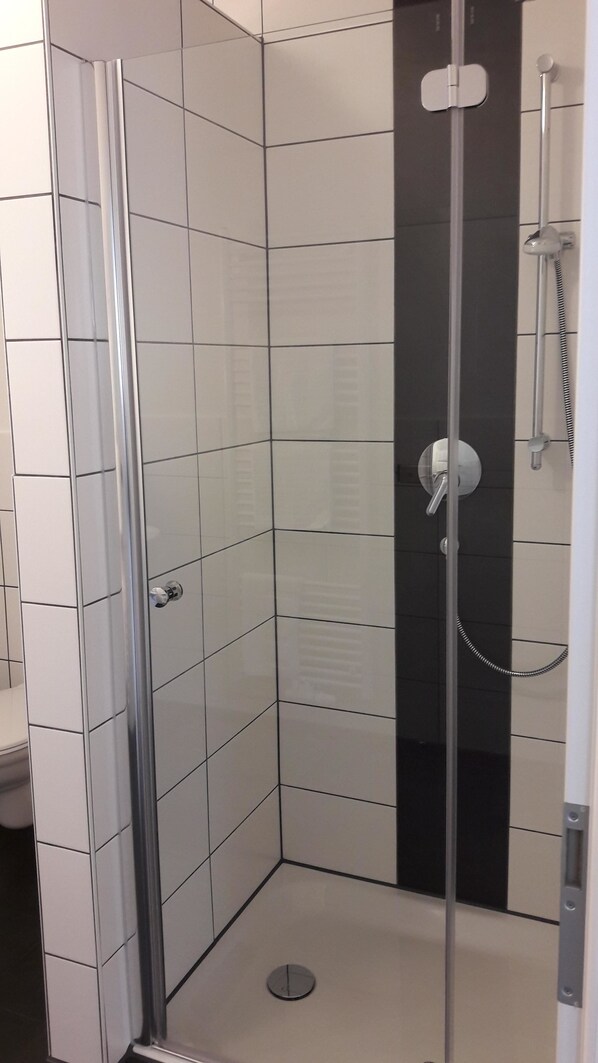 A glass-enclosed shower stall with a white tiled floor and a black vertical panel.