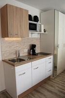 A compact kitchen with a wooden cabinet, a microwave, a coffee maker, and a sink.