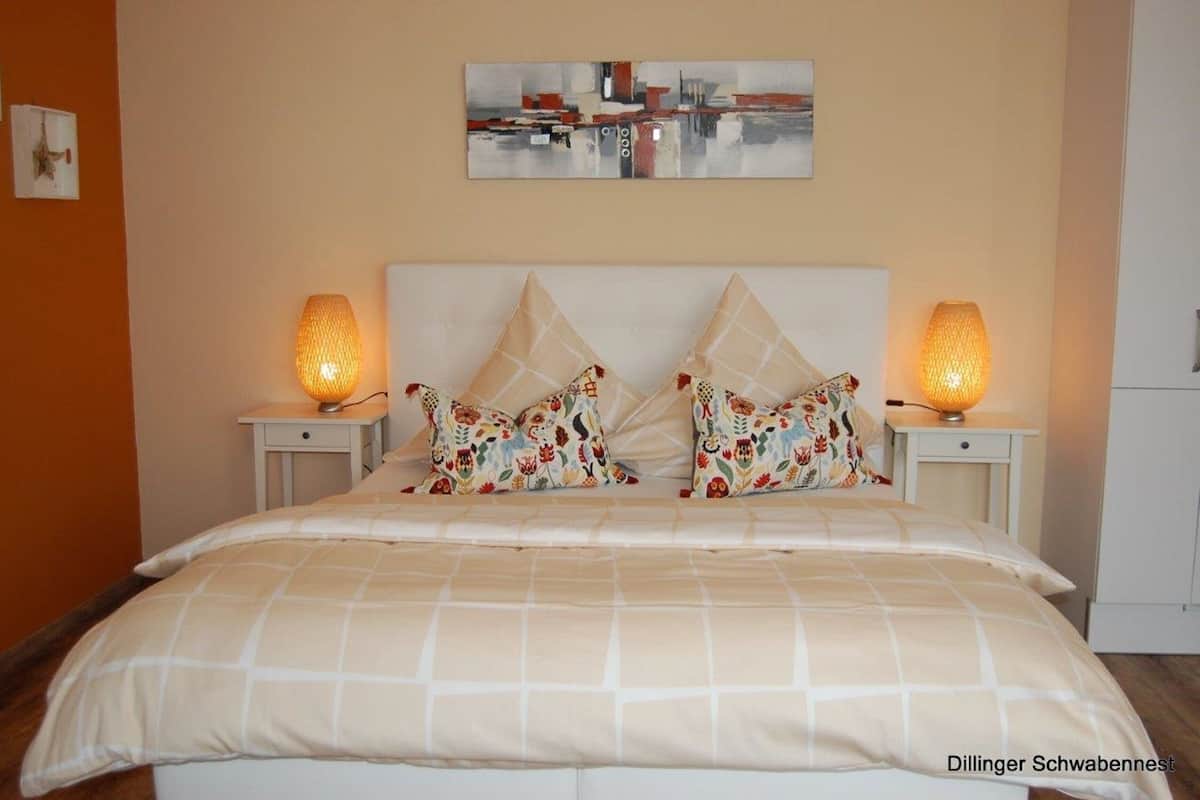 A neatly made bed with a checkered bedspread, two decorative pillows, and two bedside lamps.