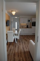 A modern kitchen with white cabinets, a microwave, and an oven. There is a dining area with a table and chairs.
