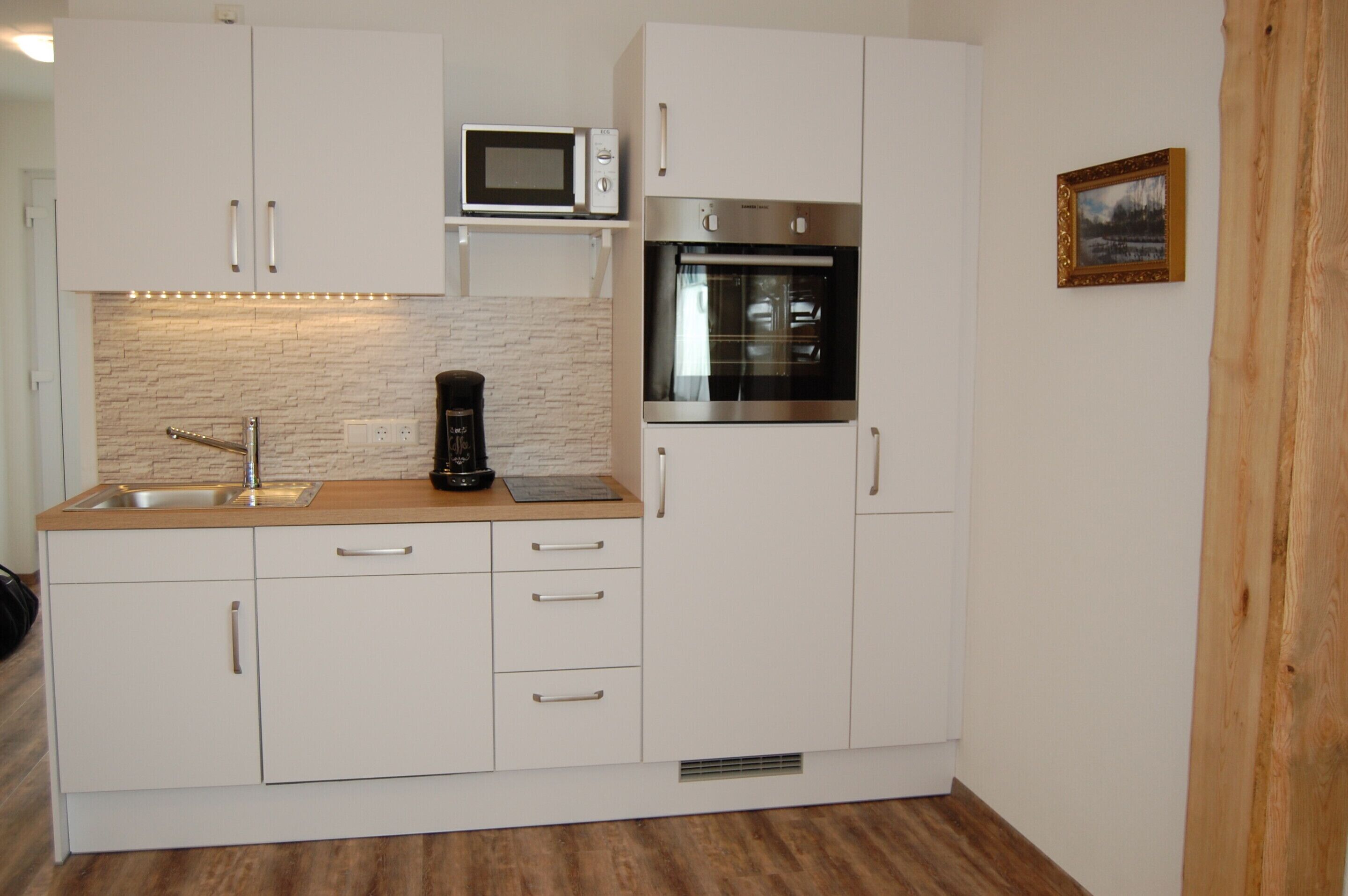 Una cocina moderna con armarios blancos, microondas integrado, horno y cafetera sobre la encimera.