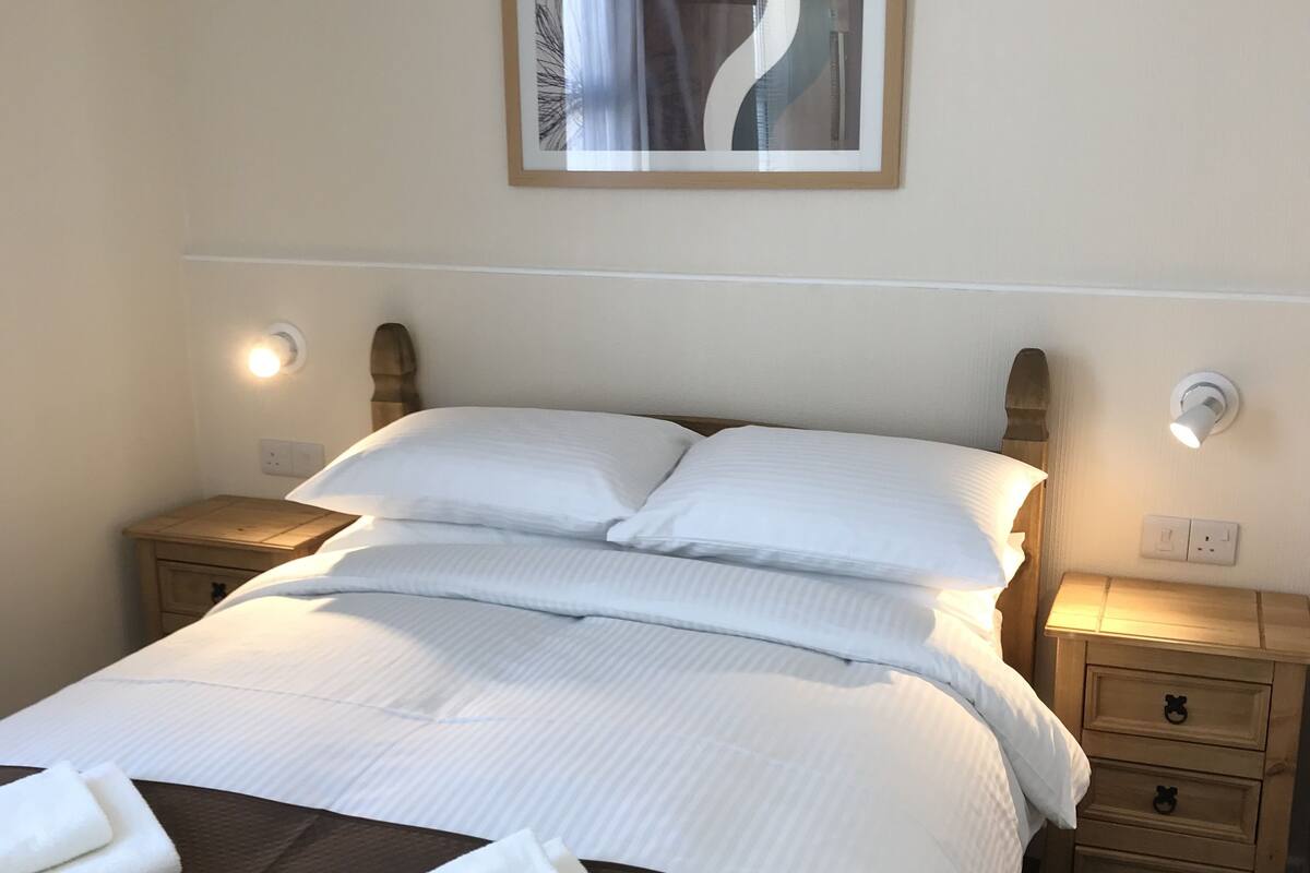 A neatly made bed with white linens, two bedside tables with lamps, and a framed abstract artwork on the wall.
