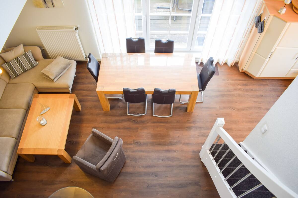 A spacious living area with a wooden dining table, black chairs, a sofa, and a small side table.