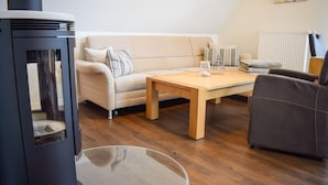 A living room with a sofa, a coffee table, and a fireplace. - Möwennest Greetsiel (Krummhoern)