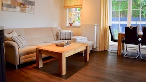 A cozy living room with a sofa, a wooden coffee table, and a dining area with chairs. - Möwennest Greetsiel (Krummhoern)