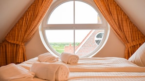 A bedroom with a large window, a bed with white linens, and a view of a brick building outside. - Möwennest Greetsiel (Krummhoern)