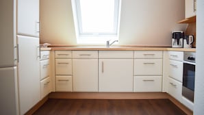 A modern kitchen with white cabinets, a wooden countertop, a built-in oven, and a window above the sink. - Möwennest Greetsiel (Krummhoern)