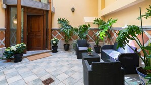 Um pátio com porta de madeira, plantas em vasos, móveis de vime e piso de azulejos.