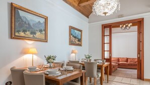 Uma sala de jantar com uma mesa de madeira posta para quatro pessoas, duas luminárias fixadas na parede e quadros com paisagens.