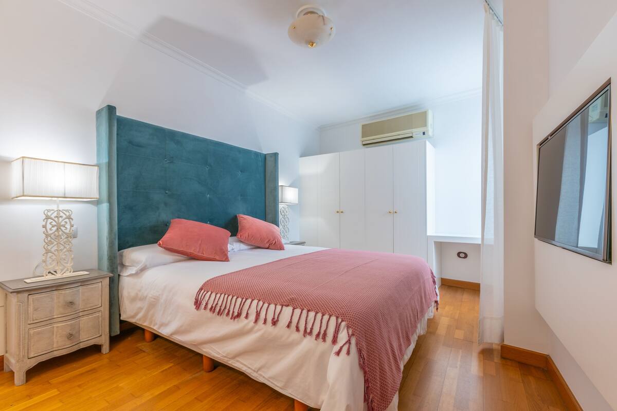 A bedroom with a bed, nightstand, wardrobe, and an air conditioning unit.
