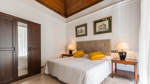 Quarto com uma cama grande, guarda-roupa de madeira, duas mesas de cabeceira com abajures e duas quadros na parede.
