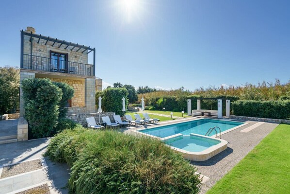 A pool with lounge chairs, a stone building with a balcony, and well-maintained greenery.
