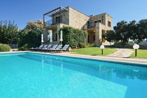 Piscina com espreguiçadeiras, um edifício de pedra com varandas e céu claro.