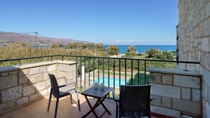 Un balcón con pared de piedra, dos sillas de mimbre, una mesita y vistas a una piscina y al mar.
