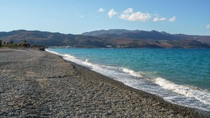 Una playa de guijarros con vistas a montañas distantes y un cielo despejado.