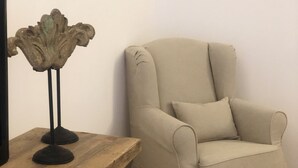 Un sillón color beige con un cojín, una mesita de madera, un objeto metálico decorativo y una cesta de mimbre.