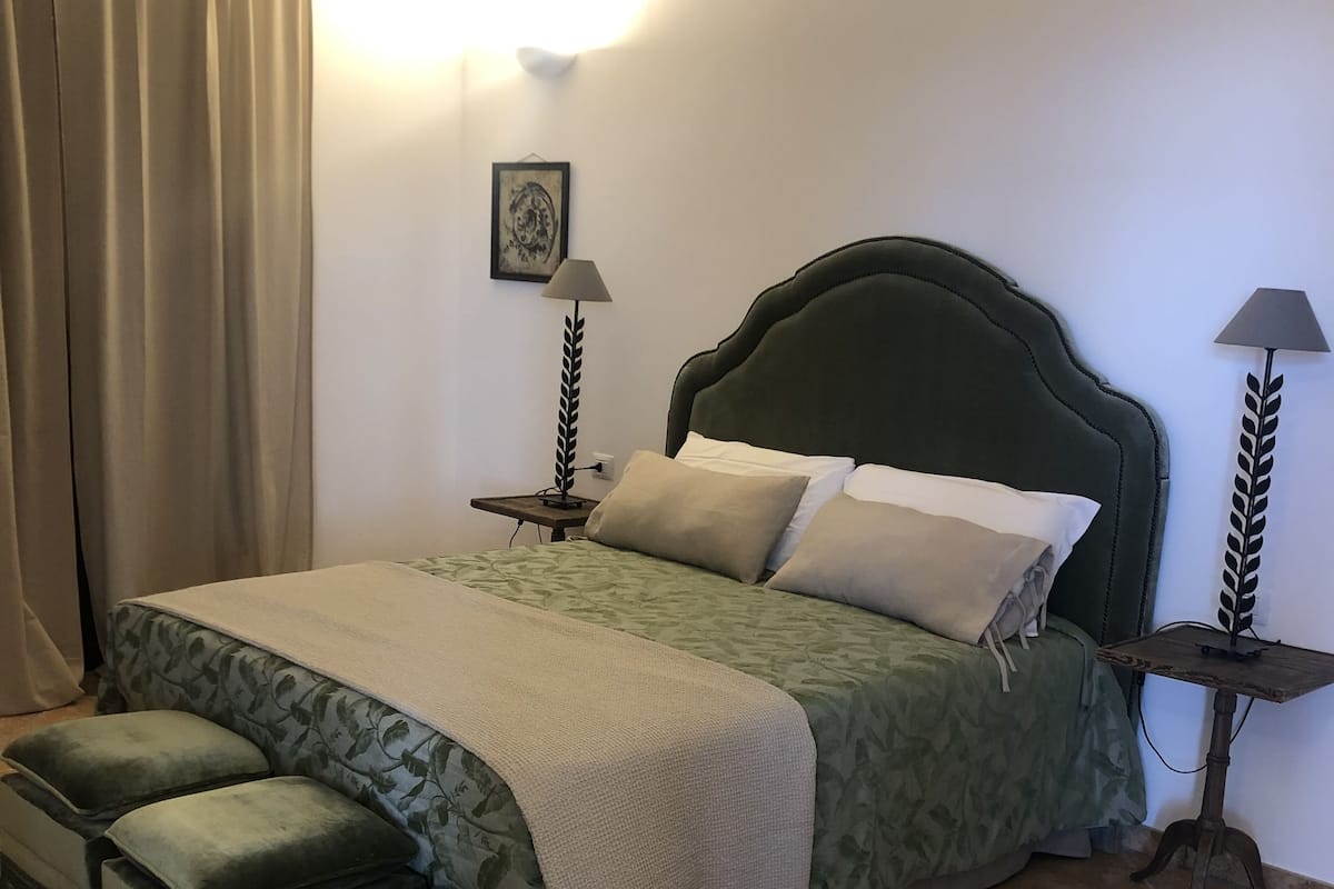 Une chambre à coucher bien rangée, avec un lit, deux tables de chevet, une lampe et un rideau.