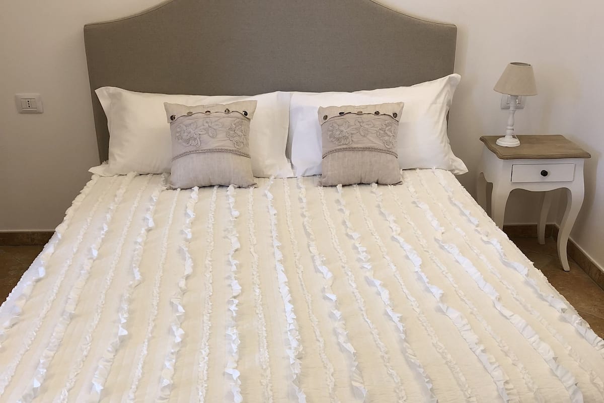 Un lit bien fait, avec une couverture blanche à volants, deux coussins décoratifs et une tête de lit.